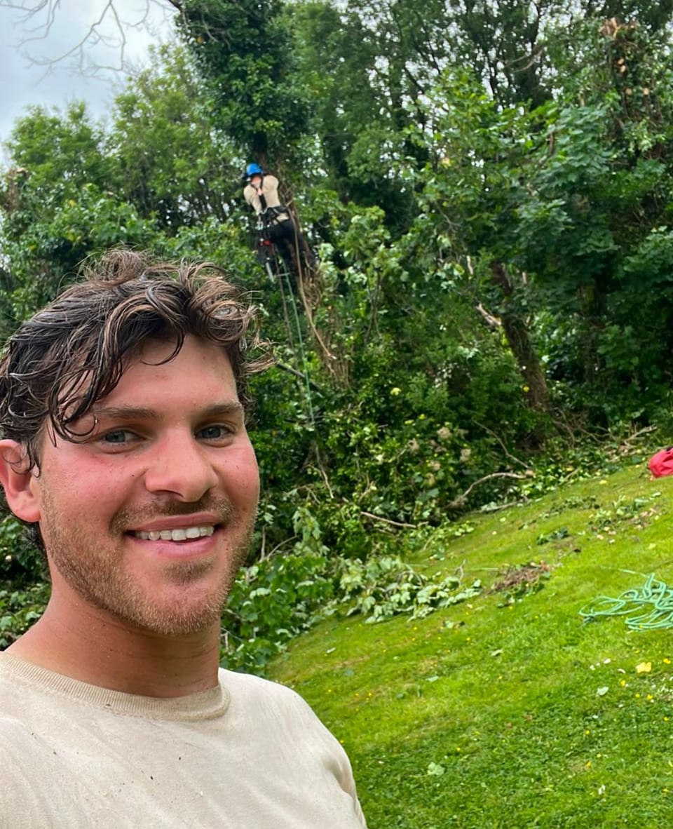 Noah Magnus on a garden job, with a climber working in the tree line behind him.